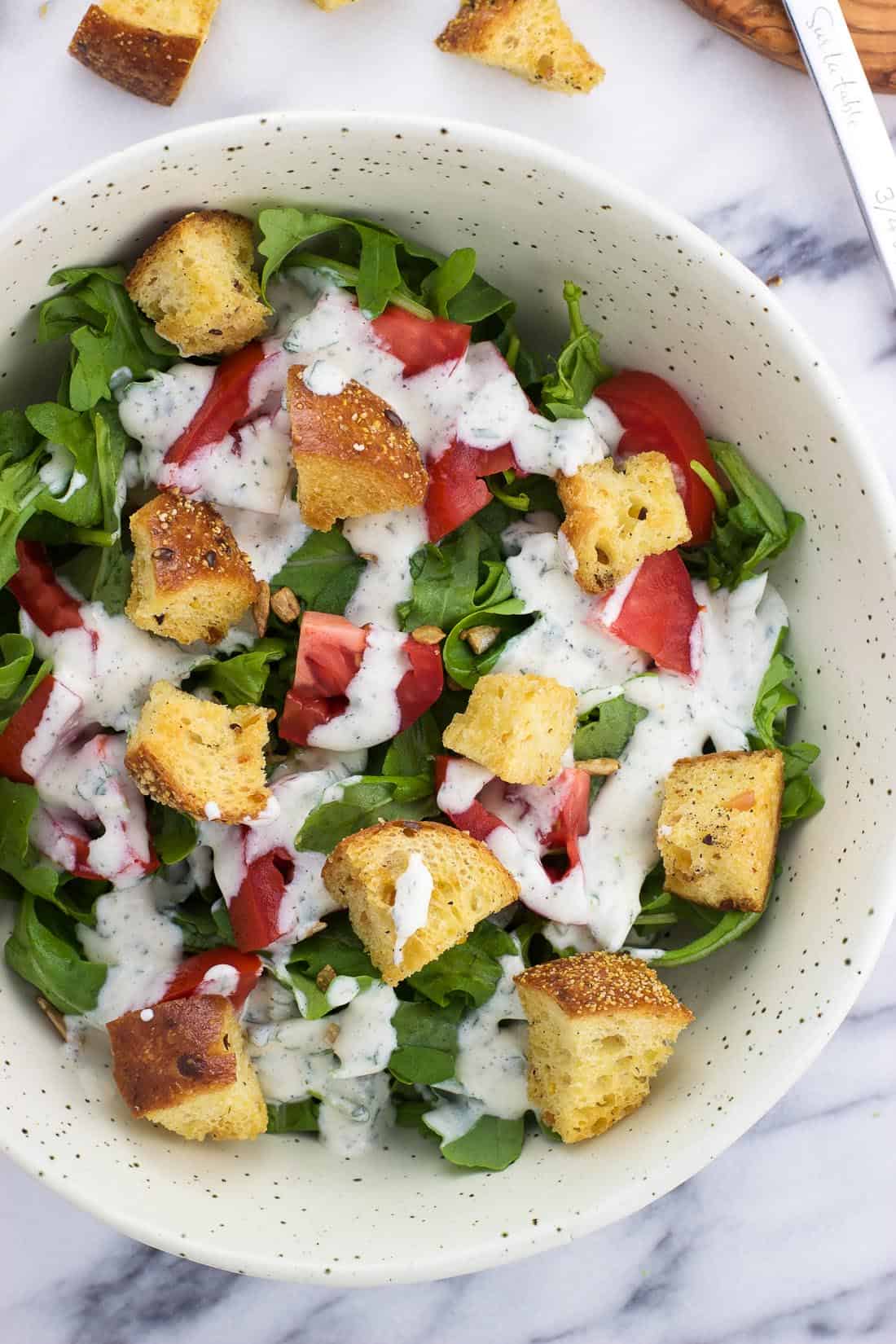 An overhead shot of a bowl of lettuce topped by chopped tomatoes, croutons, and cilantro lime ranch