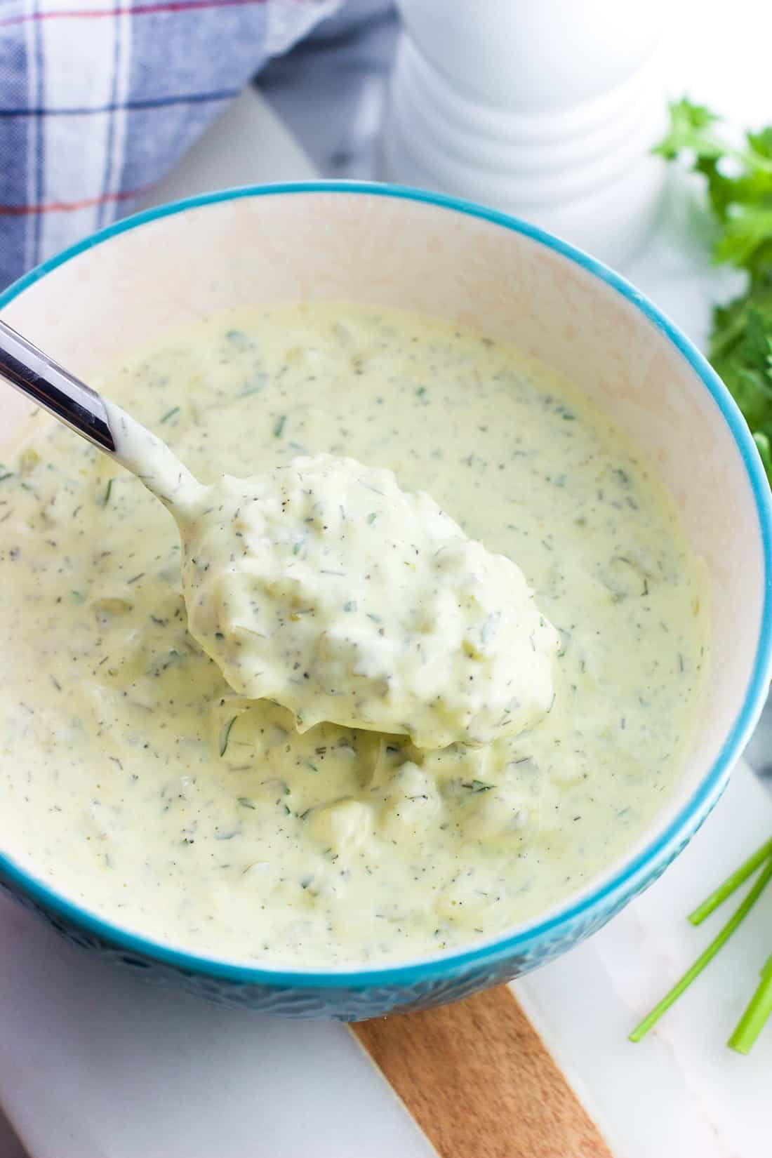 A spoon full of tartar sauce over a serving bowl.