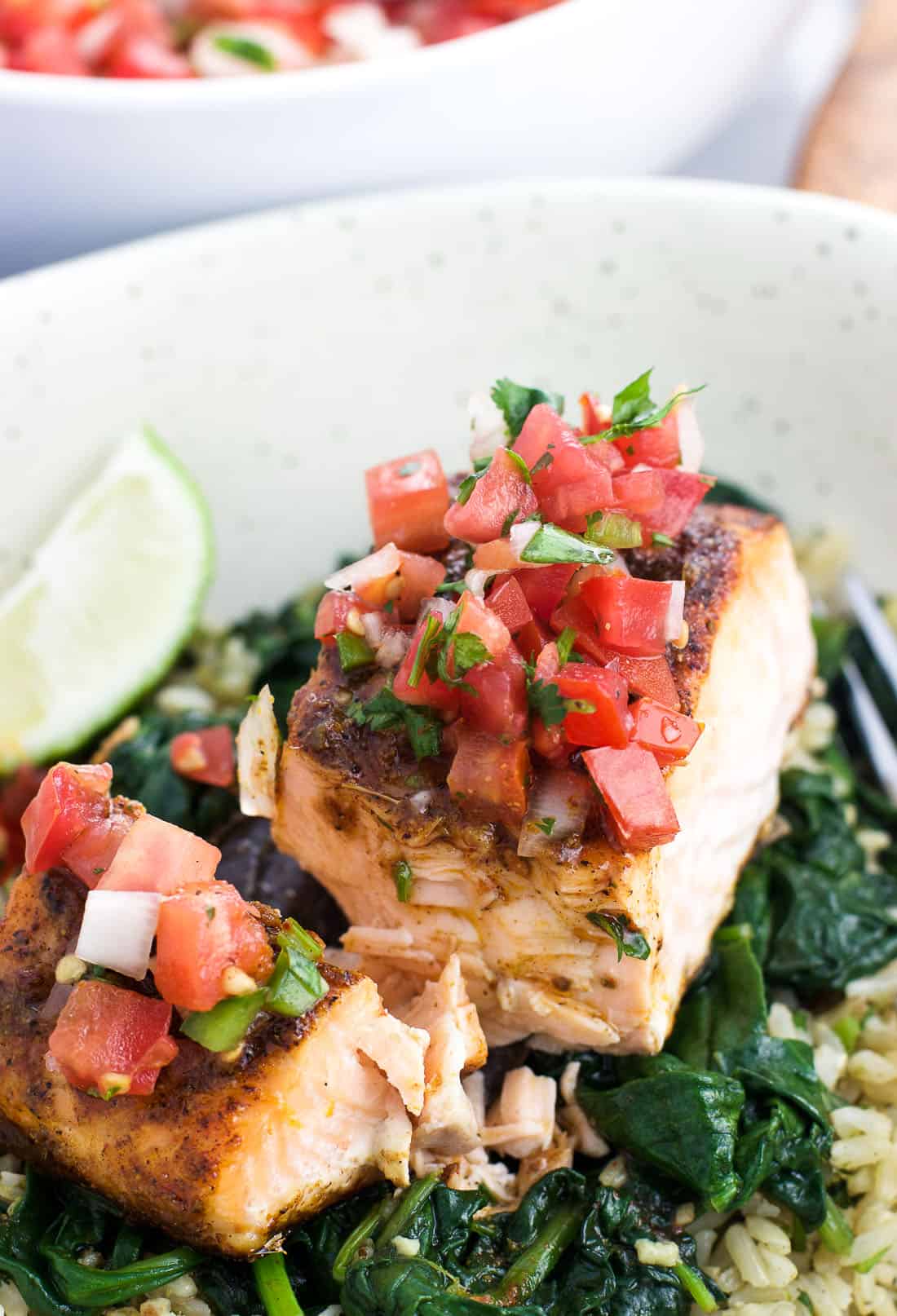 Pico de gallo on top of a baked salmon fillet on a bed of spinach and rice in a bowl.