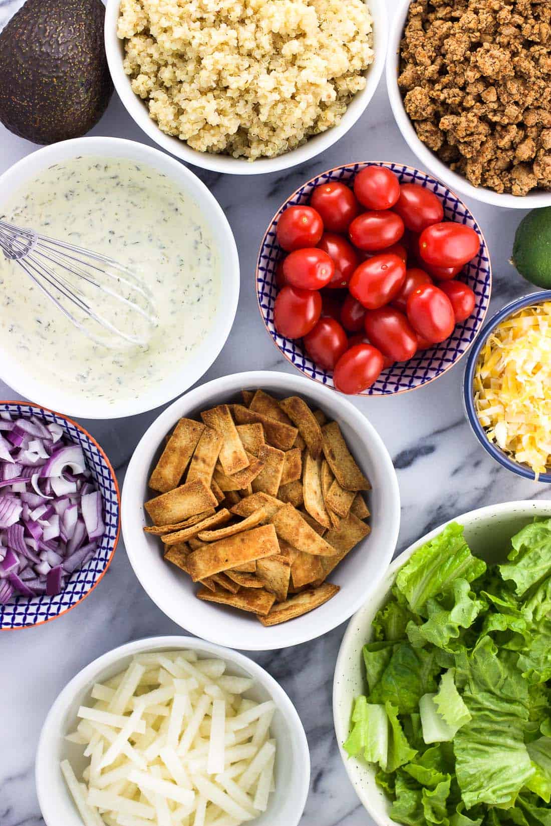 An overhead shot of the salad ingredients on a marble bowl, including cooked ground turkey, vegetables, quinoa, dressing, and tortilla strips