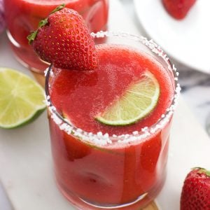 A strawberry ginger margarita in a glass with a salted rim and a strawberry and a lime wedge for garnish