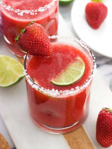 A strawberry ginger margarita in a glass with a salted rim and a strawberry and a lime wedge for garnish