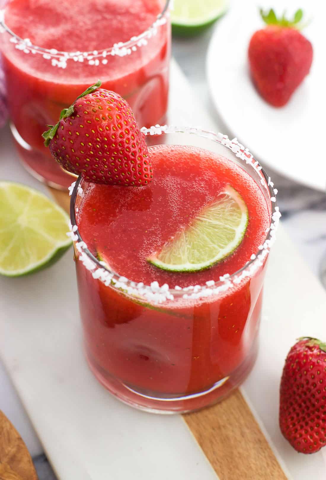 A fresh strawberry ginger margarita in a glass with a salted rim and a strawberry and a lime wedge for garnish