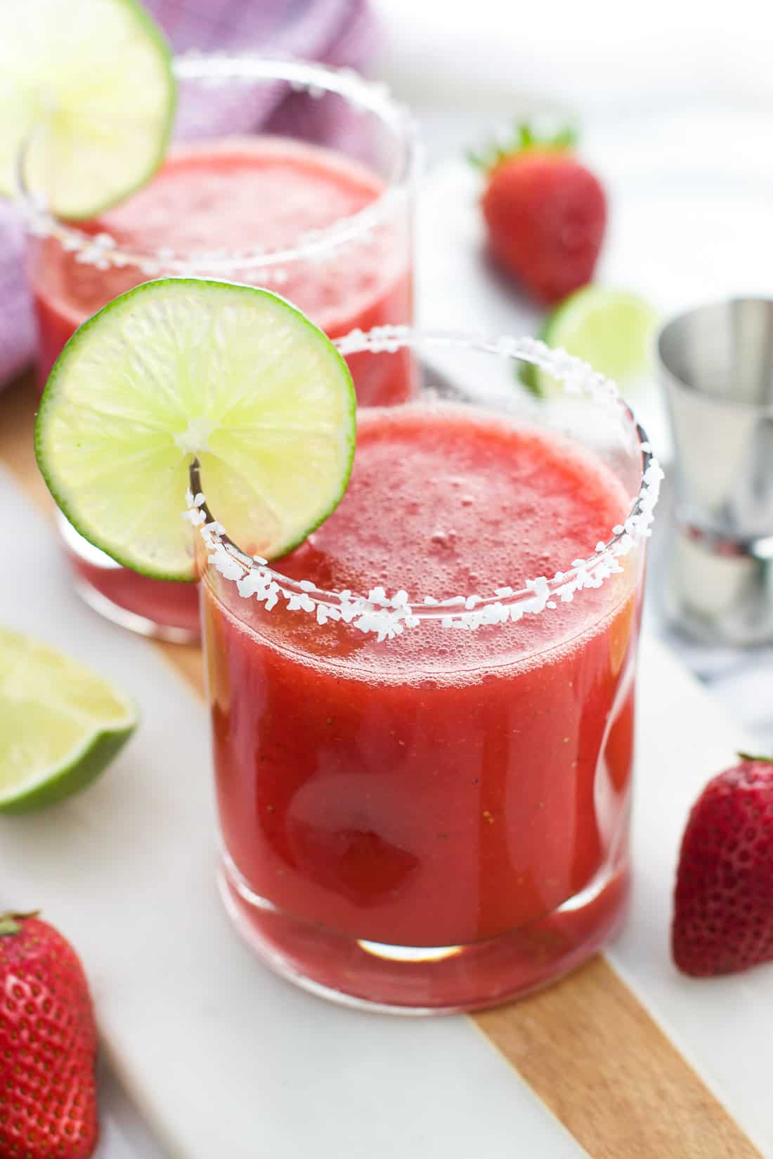 A strawberry ginger margarita in a glass with a salted rim and a lime round as garnish