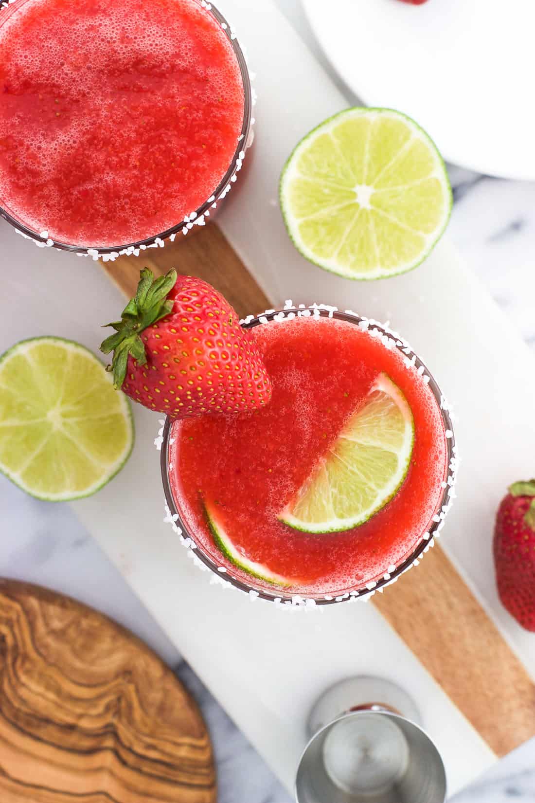 An overhead shot of two strawberry ginger margaritas on a marble board garnished with strawberries and limes