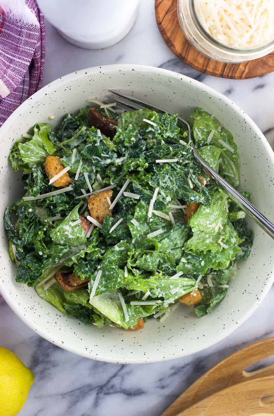 An overhead shot of kale caesar salad in a bowl with a fork.