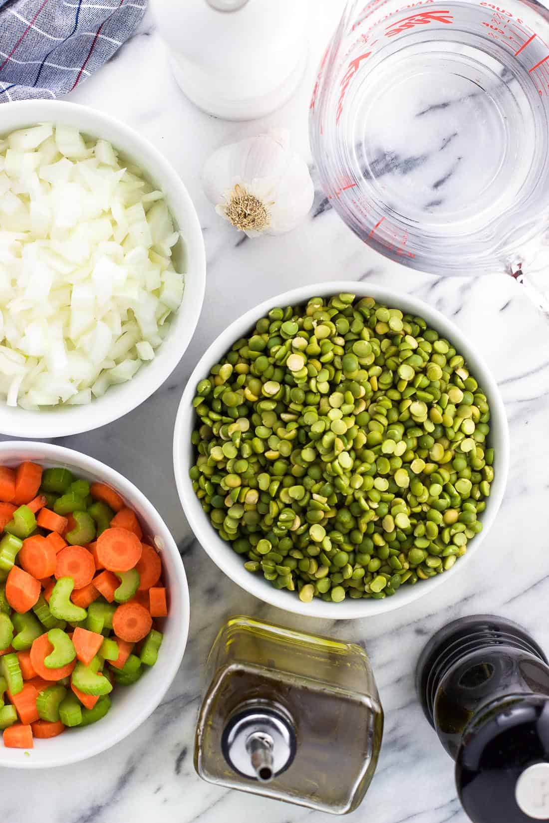 Split pea soup ingredients on a marble board, including dried split peas, carrots, celery, onion, garlic, oil, and spices.