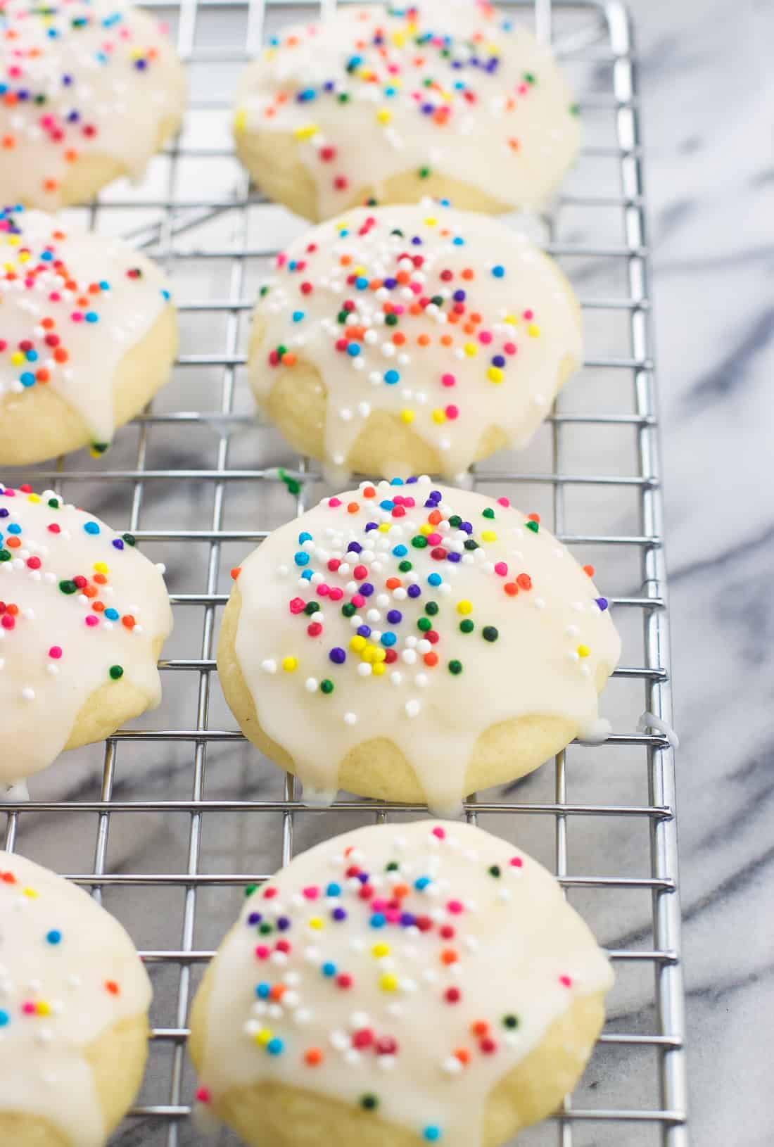 Iced and sprinkled Italian ricotta cookies on a wire rack.