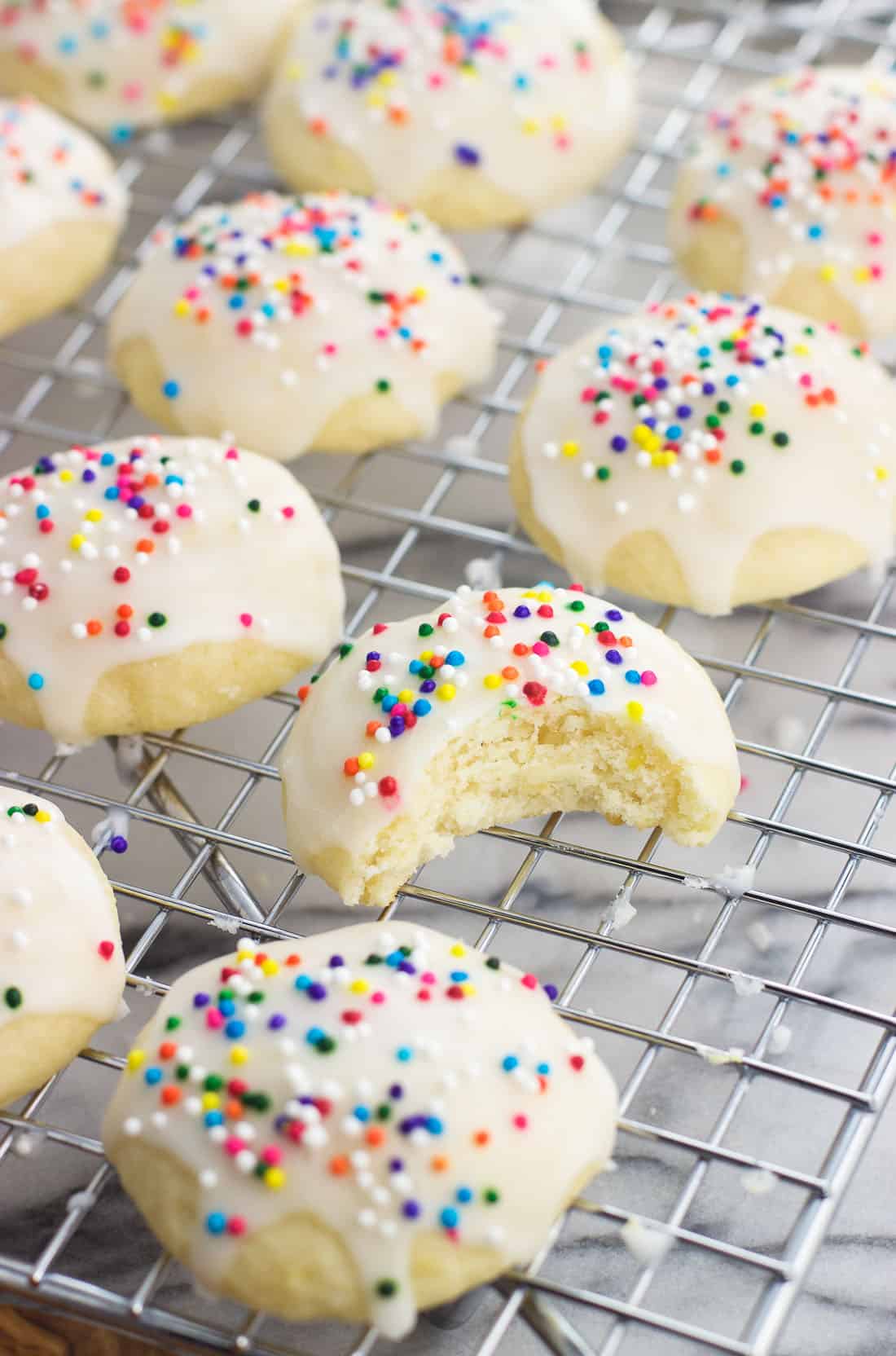 Iced Italian ricotta cookies on a wire rack with a bite taken out of one