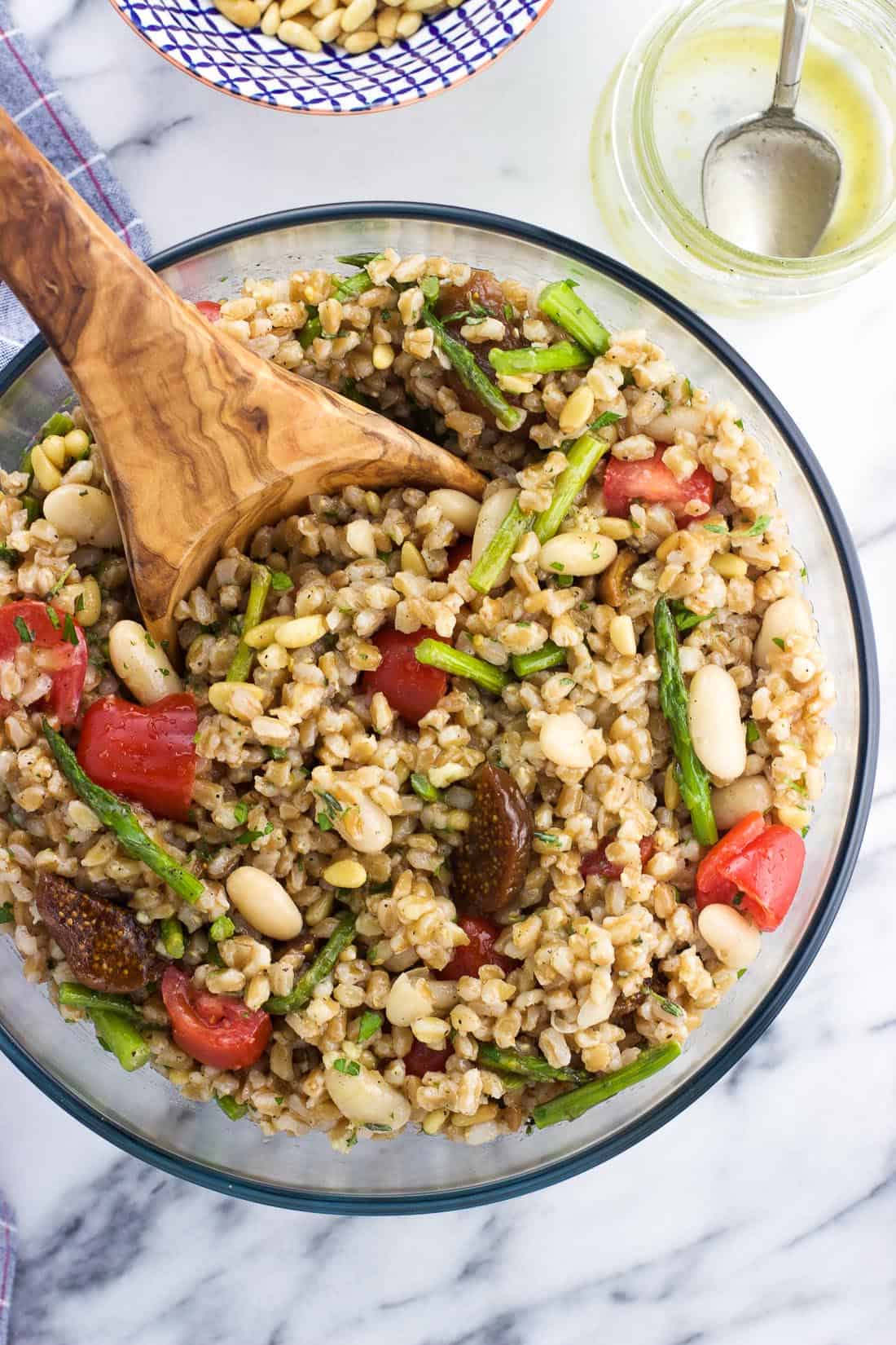 An overhead shot of the assembled farro and bean salad in a serving bowl with a wooden serving spoon.