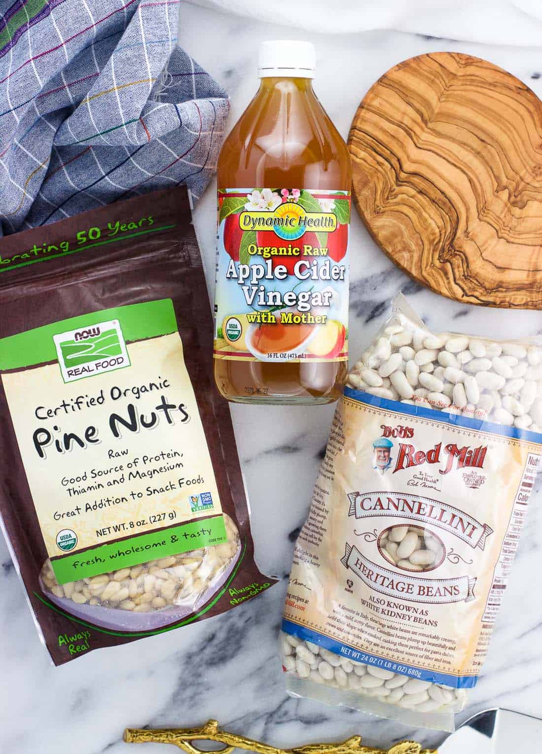 An overhead shot of ingredients from iHerb: pine nuts, apple cider vinegar, and cannellini beans.