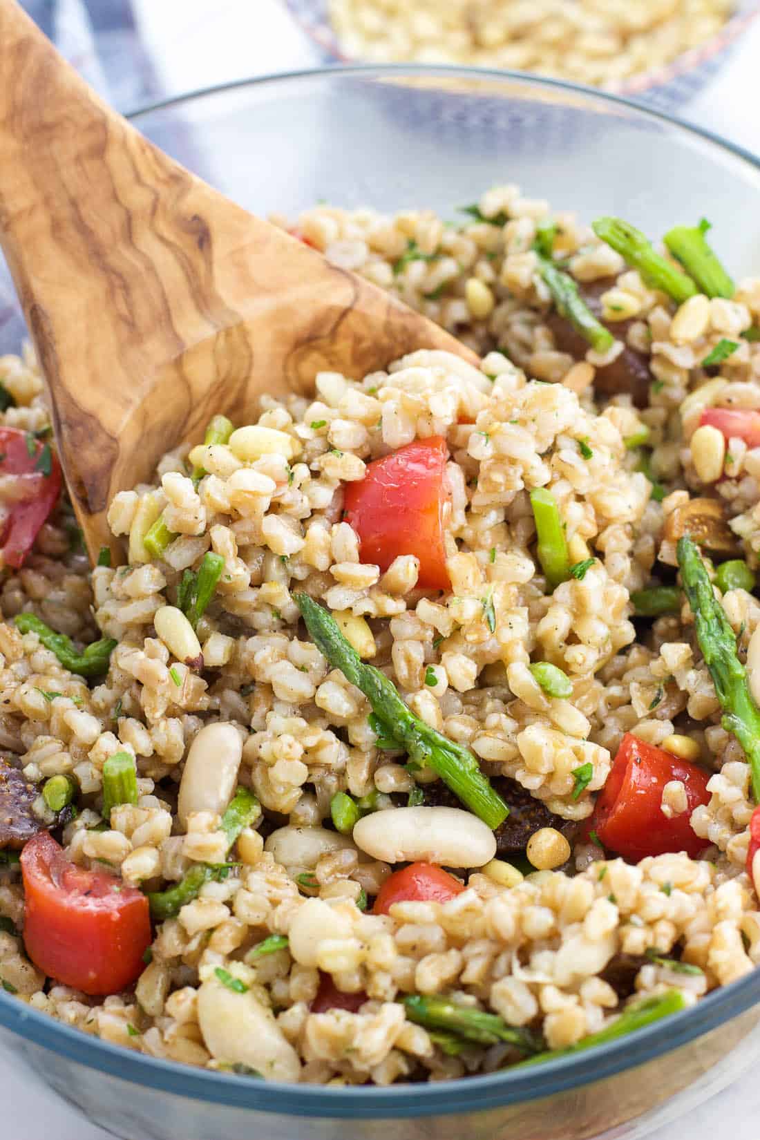 A wooden serving spoon scooping out a portion of farro salad from a serving bowl.