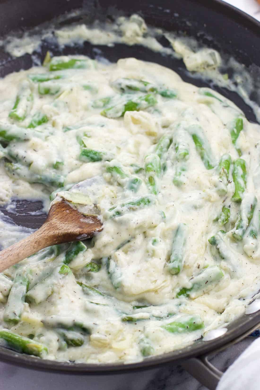 The thickened quiche mixture featuring asparagus in a saucepan with a wooden spoon.