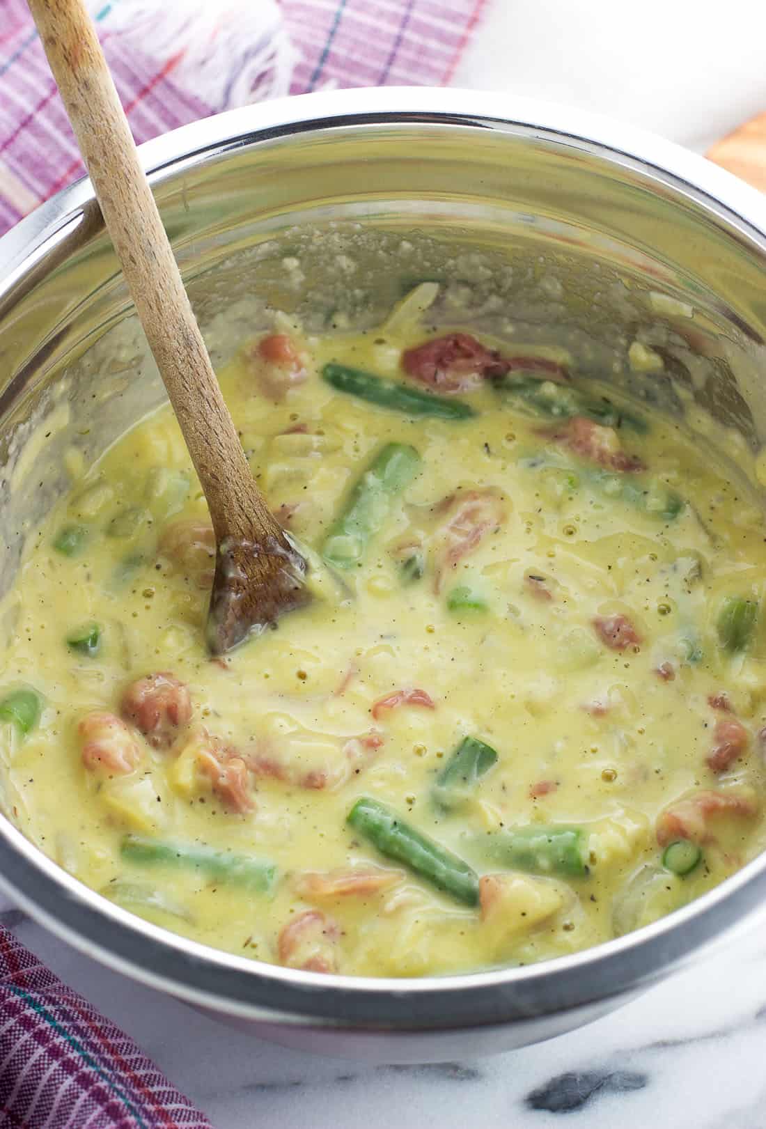 Eggs and the other quiche filling ingredients stirred together in a metal mixing bowl with a wooden spoon