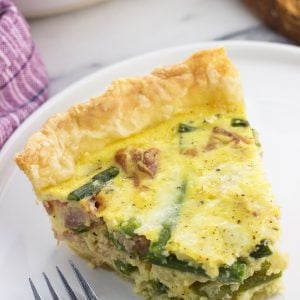 A slice of quiche on a plate with a bite taken out next to a fork