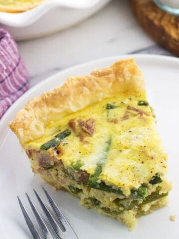 A slice of quiche on a plate with a bite taken out next to a fork
