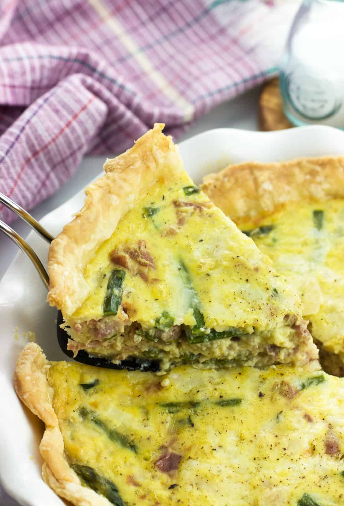 A slice of quiche being lifted out of the pie plate with a wedge-shaped spatula.