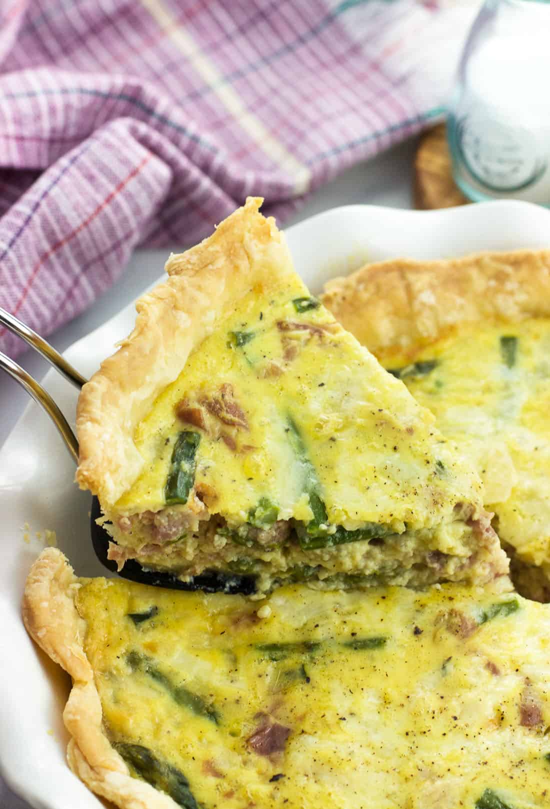 A slice of quiche being lifted out of the pie plate with a wedge-shaped spatula