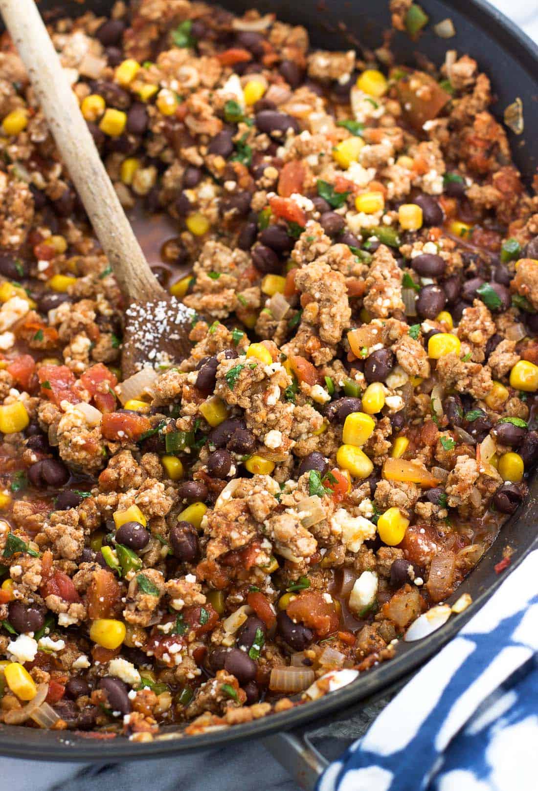 Turkey, black beans, corn, salsa, cilantro, and cotija cheese stirred together in a pan with a wooden spoon.