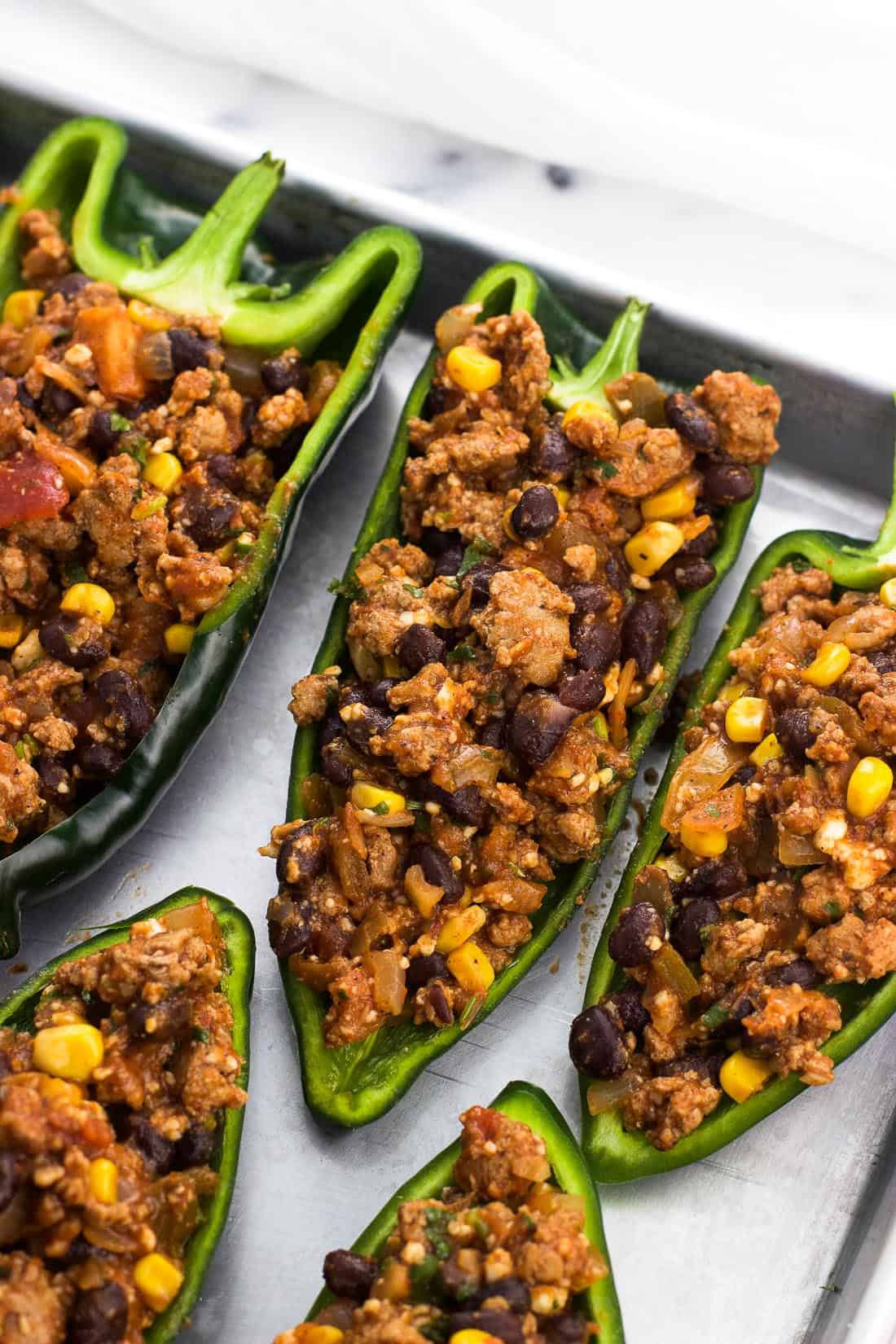 Stuffed poblano peppers on a metal baking sheet before being topped with cheese.