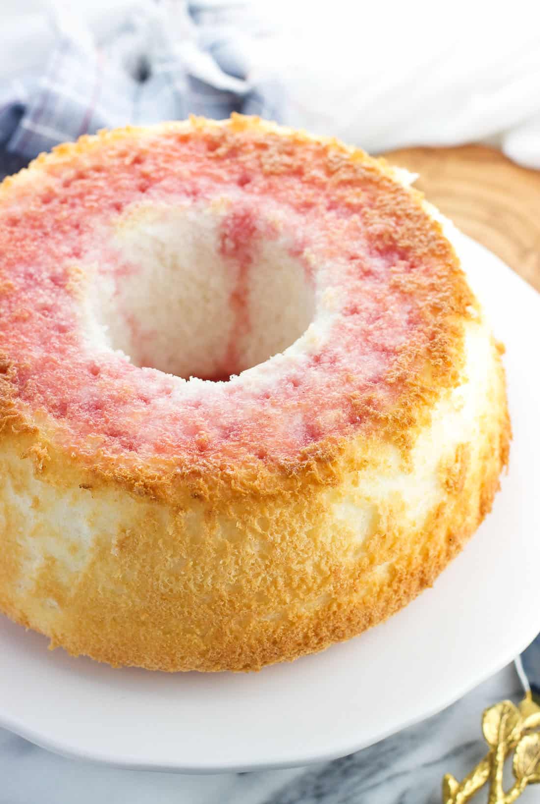 Angel food poke cake on a cake plate with strawberry syrup used as the liquid