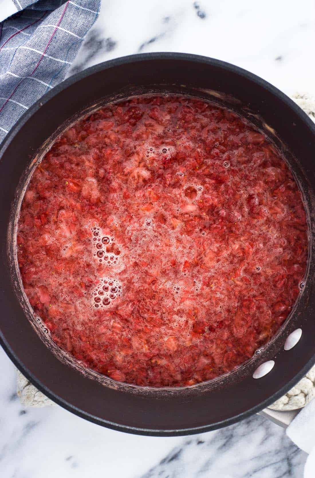 An overhead shot of water, honey, dissolved sugar, cinnamon, and mashed strawberries in a saucepan before straining