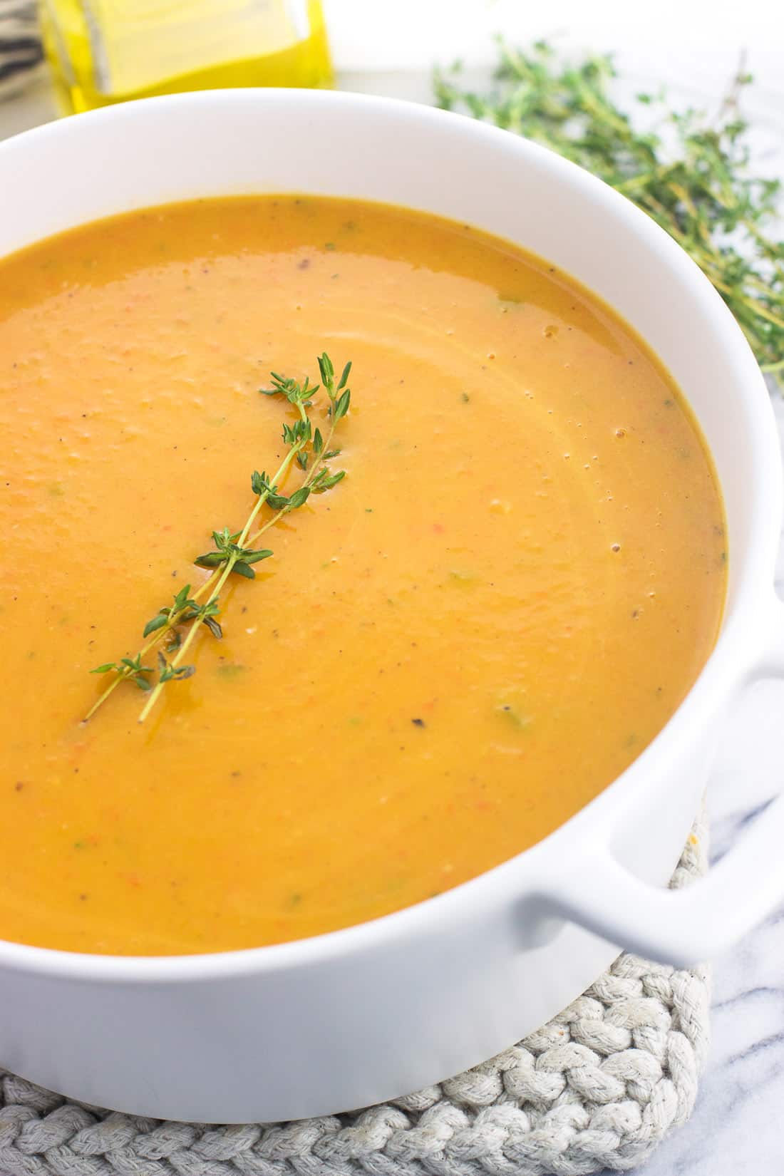 Butternut squash soup in a soup pot garnished with a sprig of thyme.