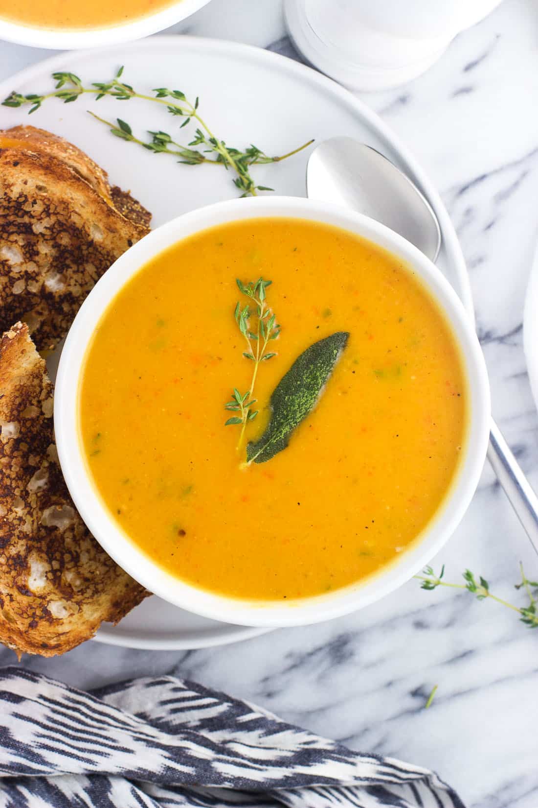 A bowl of butternut squash soup topped with herbs next to a grilled cheese sandwich.