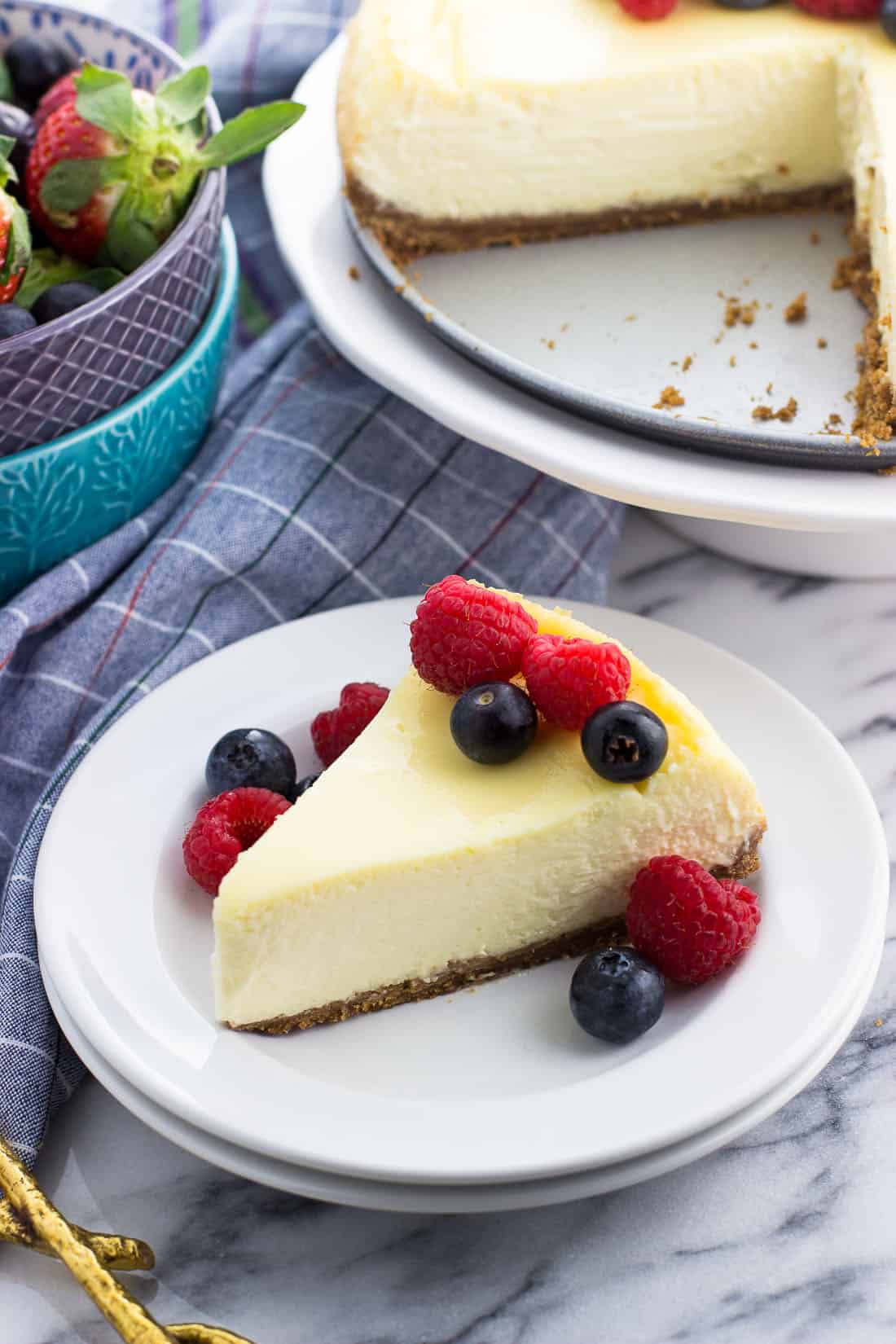 Sour cream cheesecake garnished with berries on a plate next to more fresh fruit