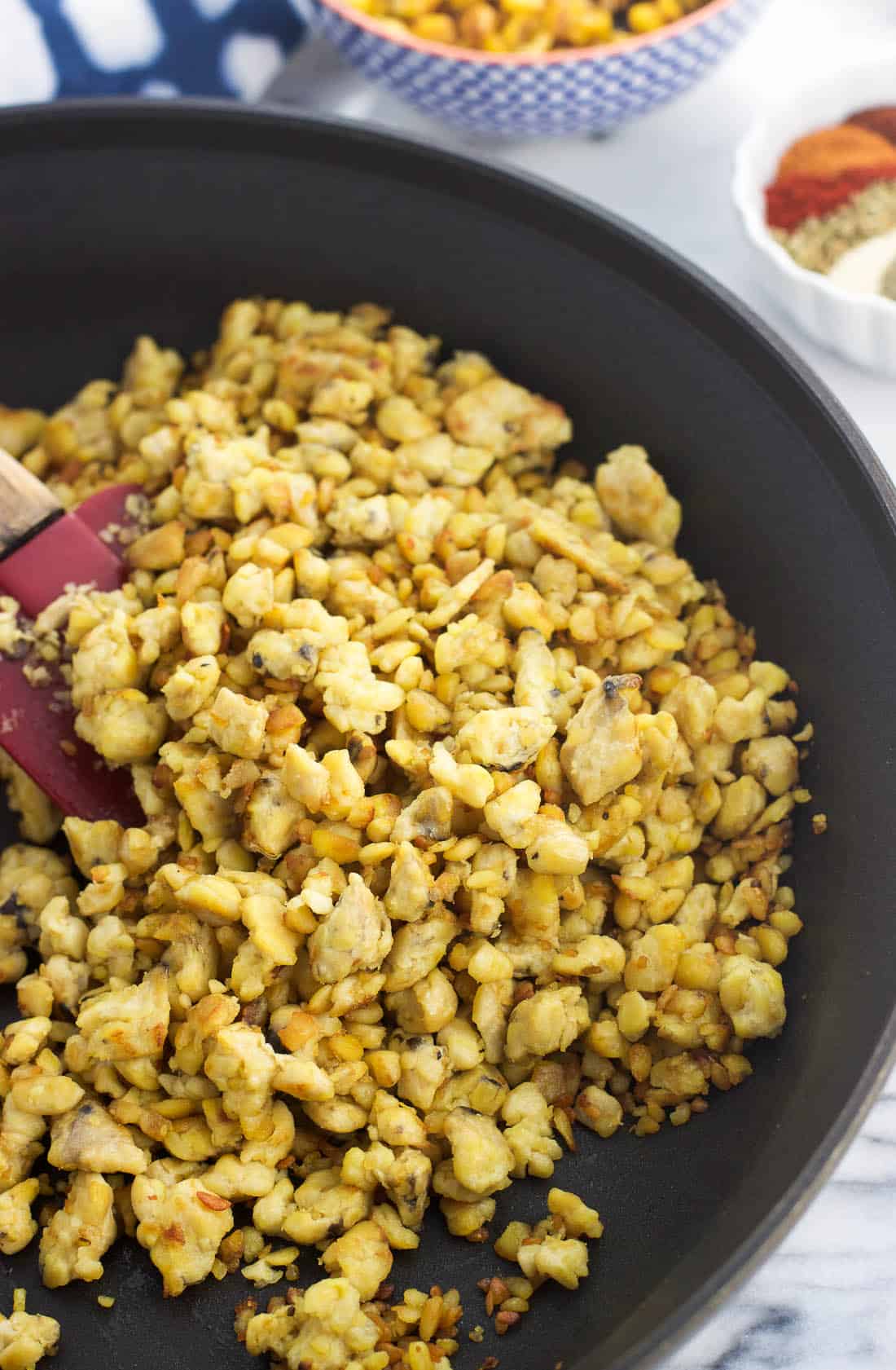 Crumbled and cooked tempeh in a pan with a spatula.