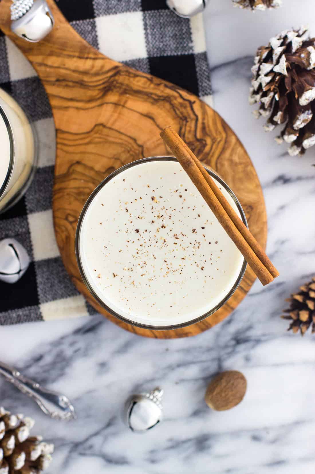 An overhead shot of a glass of eggnog dusted with grated nutmeg and garnished with a cinnamon stick