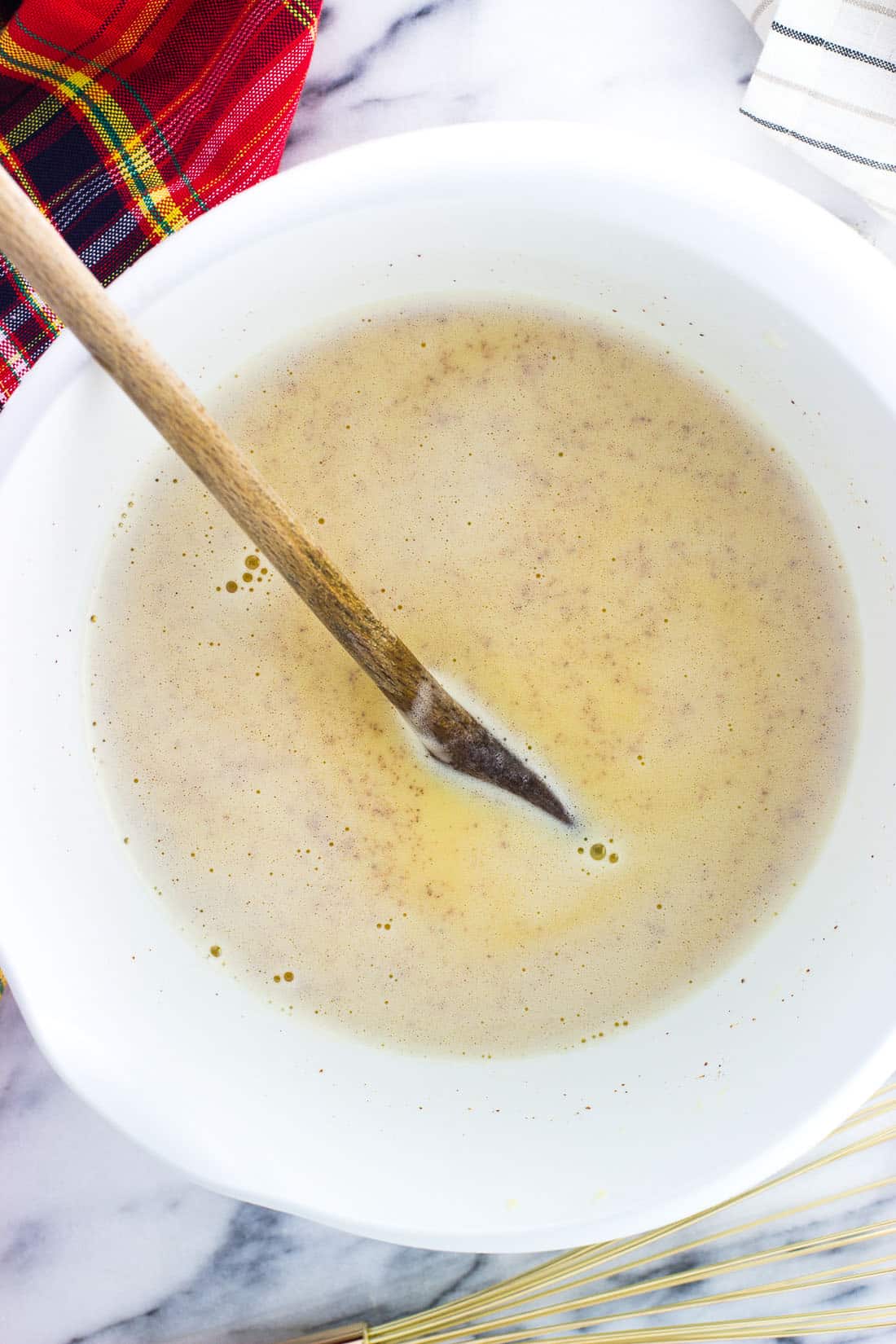 Cooked eggnog mixture partway through the recipe in a big plastic bowl with a wooden spoon