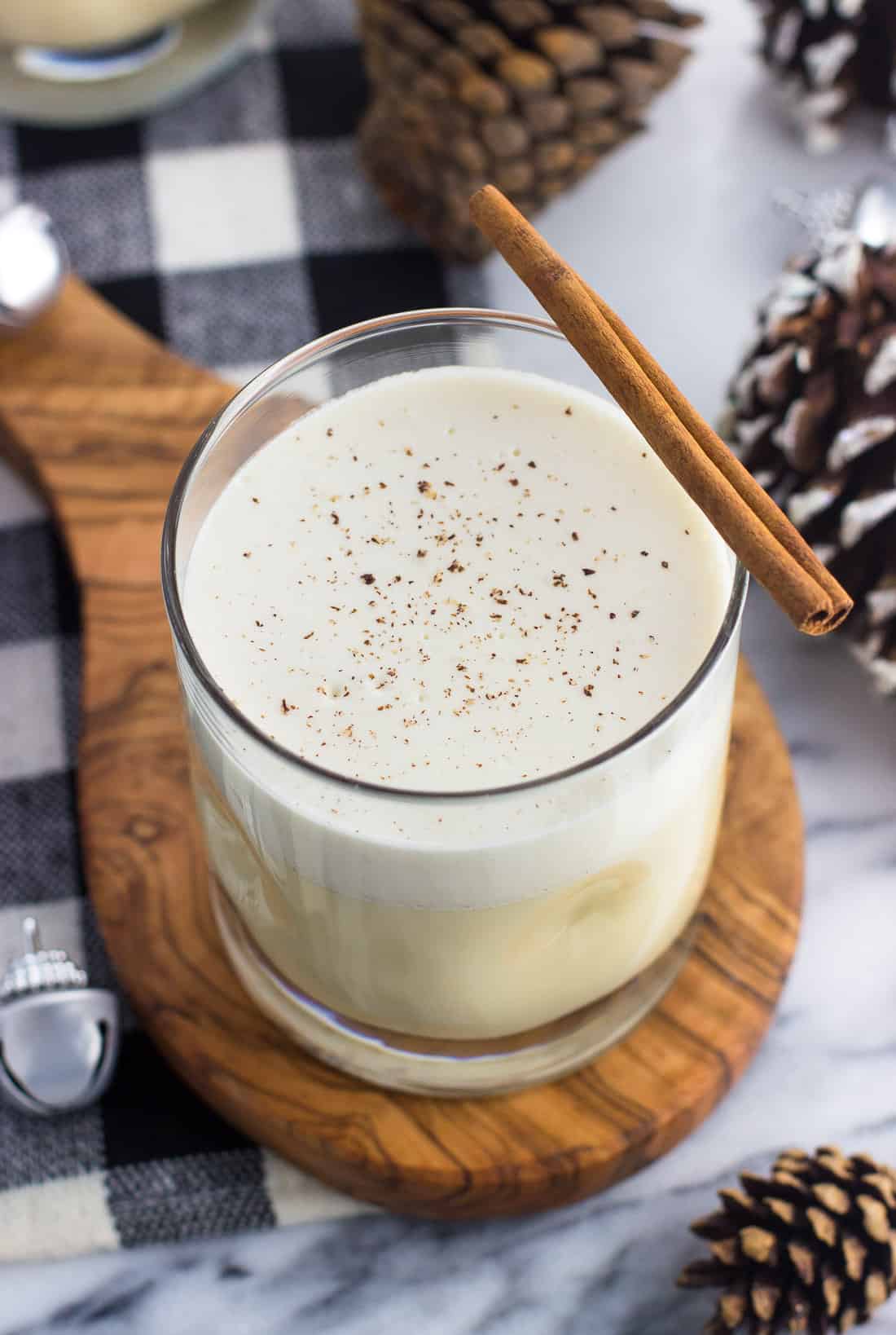 A glass of cooked eggnog on a wooden board garnished with a cinnamon stick