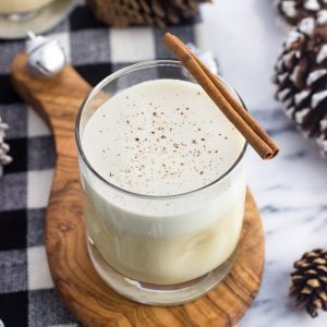 A glass of cooked eggnog on a wooden board garnished with a cinnamon stick