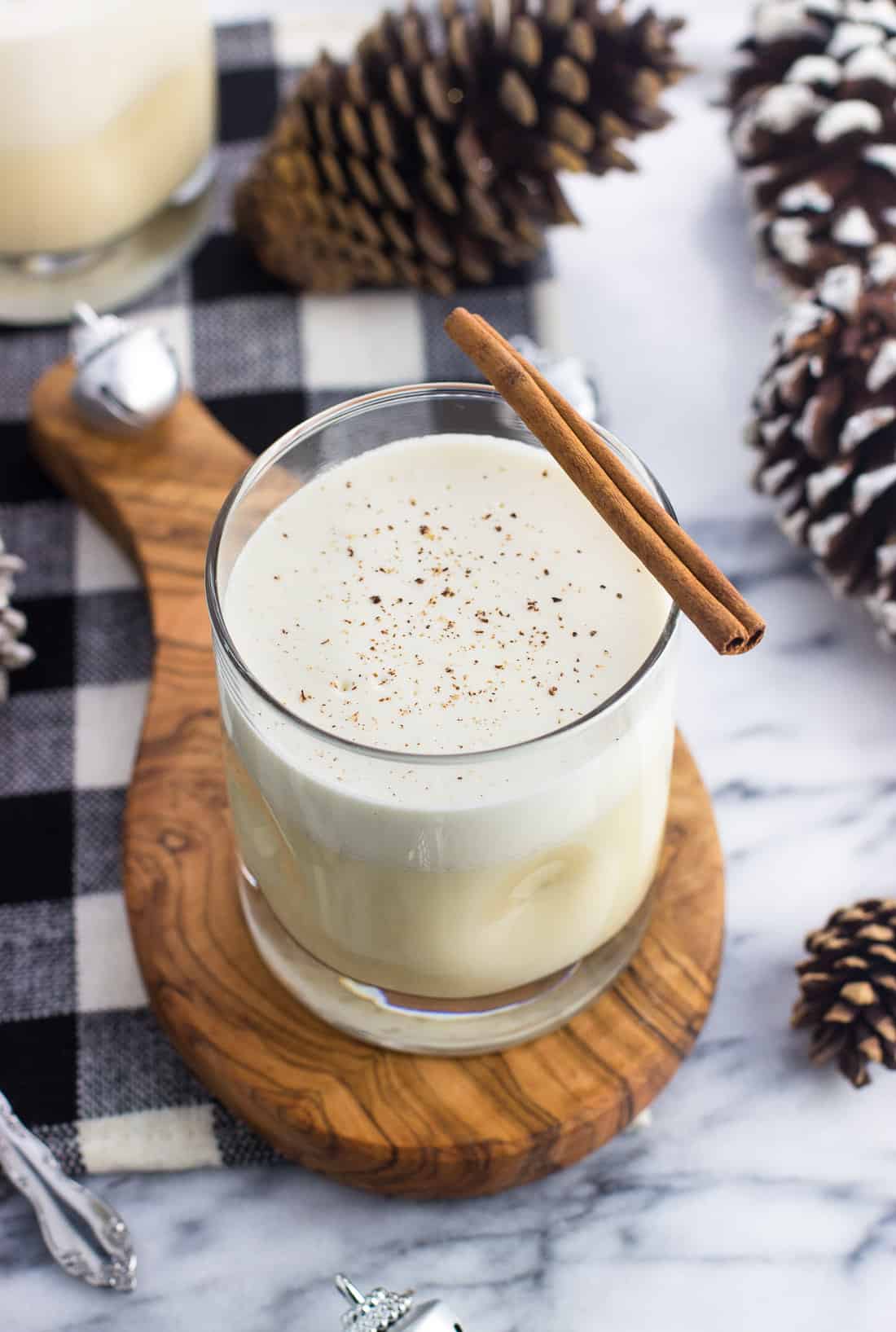 A glass of cooked eggnog on a wooden board garnished with a cinnamon stick