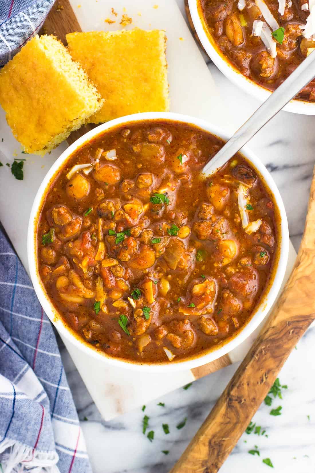 An overhead shot of a bowl of Instant Pot turkey chili with a spoon next to two pieces of cornbread for serving