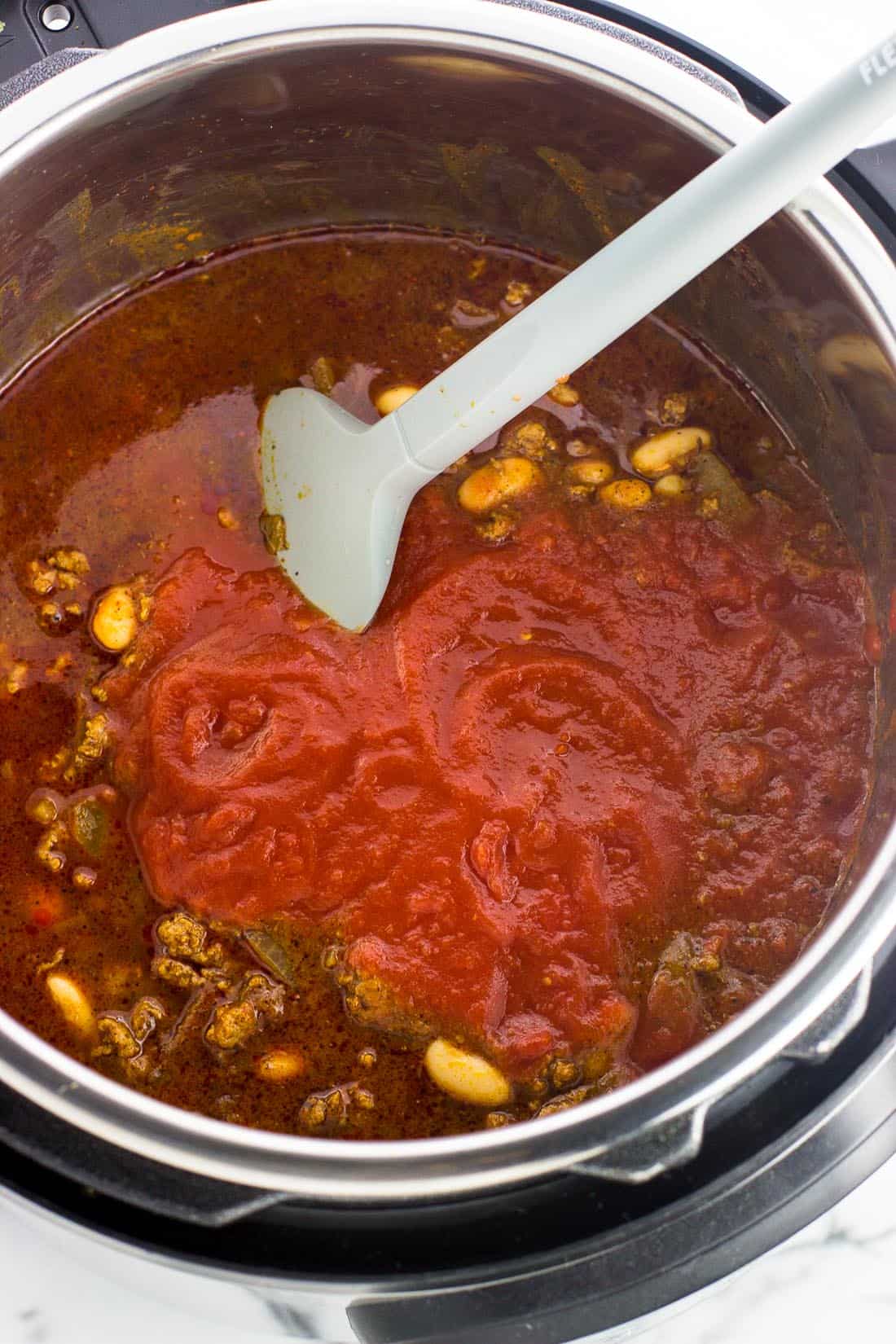 Turkey chili ingredients in the Instant Pot before cooking, with the crushed tomatoes in a layer on top