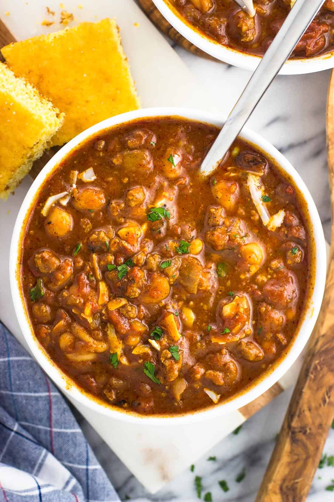 A bowl of turkey chili next to pieces of cornbread