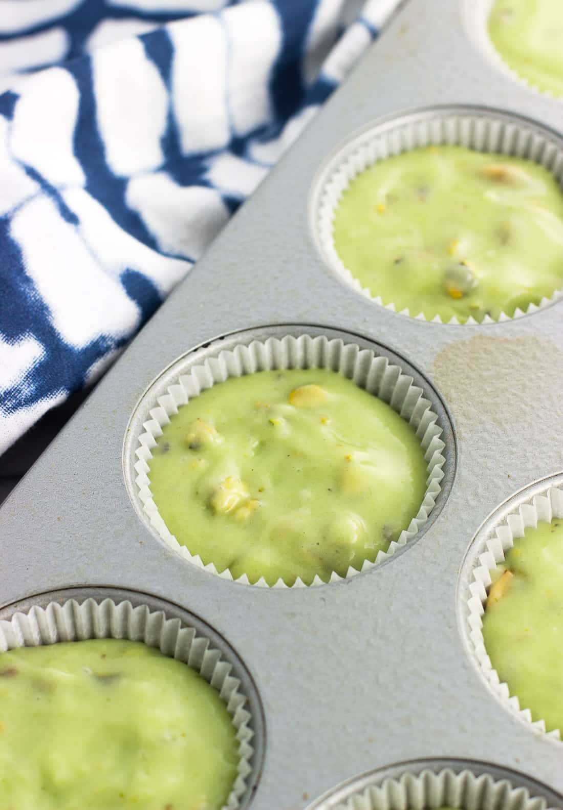 Pistachio muffin batter in muffin papers in a metal muffin tin