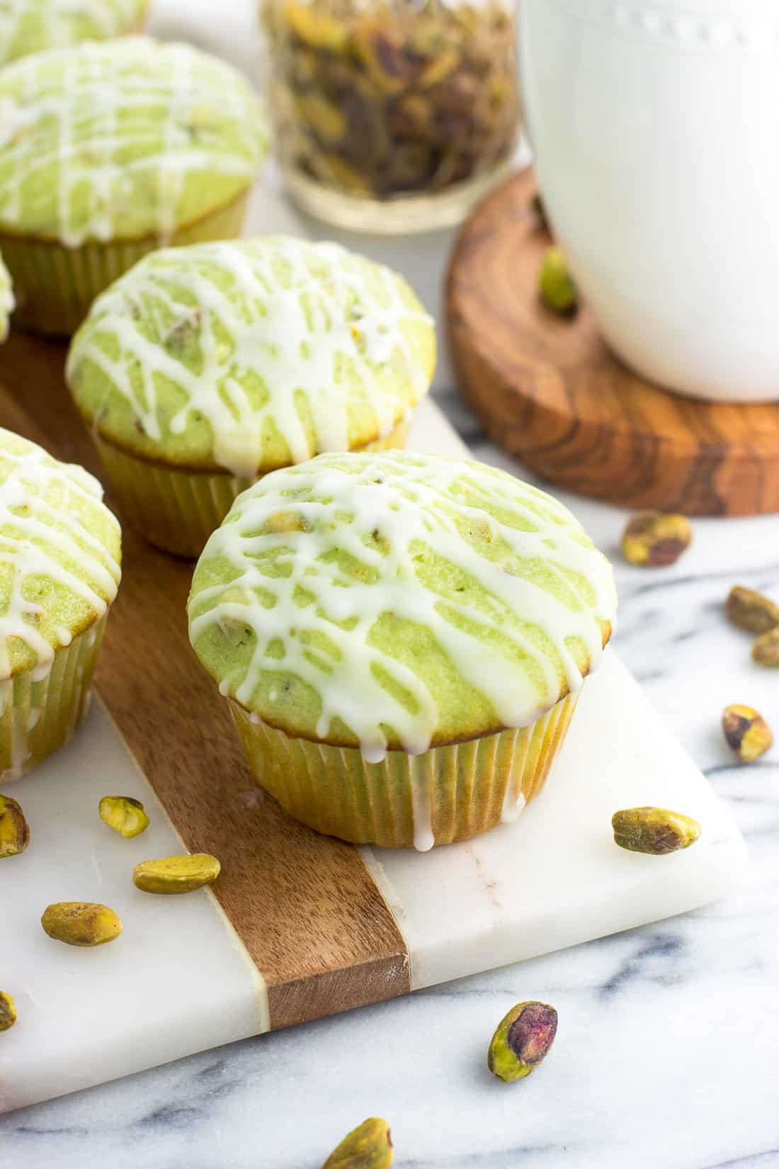 A pistachio muffin on a marble board next to a cup of coffee