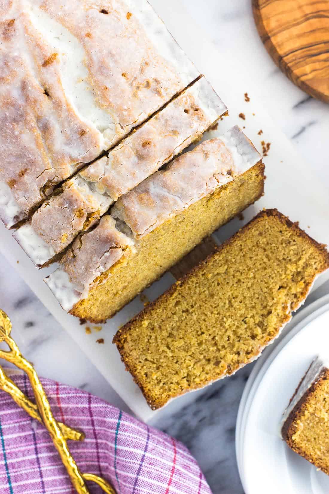 A loaf of glazed pound cake on a marble board cut into slices.