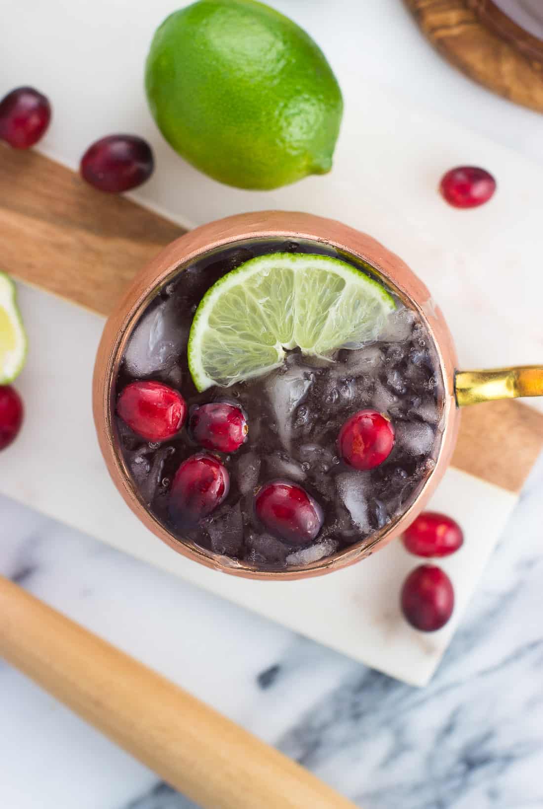 An overhead shot of a cranberry moscow mule in a copper mug on a marble serving tray