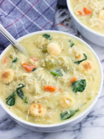 A big bowl of soup topped with oyster crackers with a big spoon