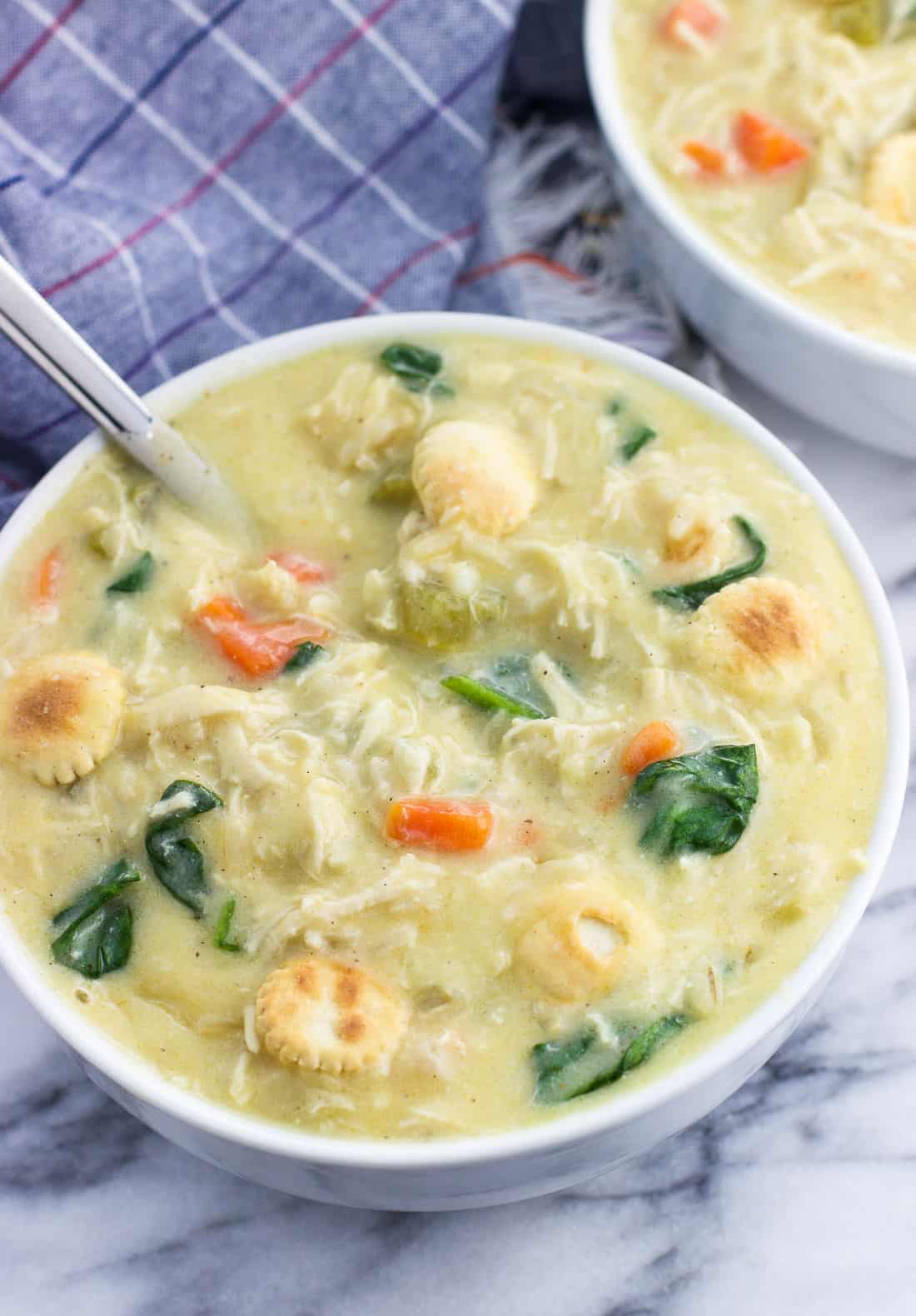 A big bowl of soup topped with oyster crackers with a big spoon.