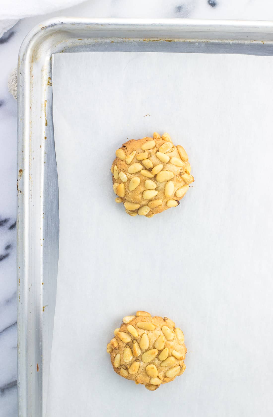 An overhead shot of a baked pignoli cookie on a baking sheet.