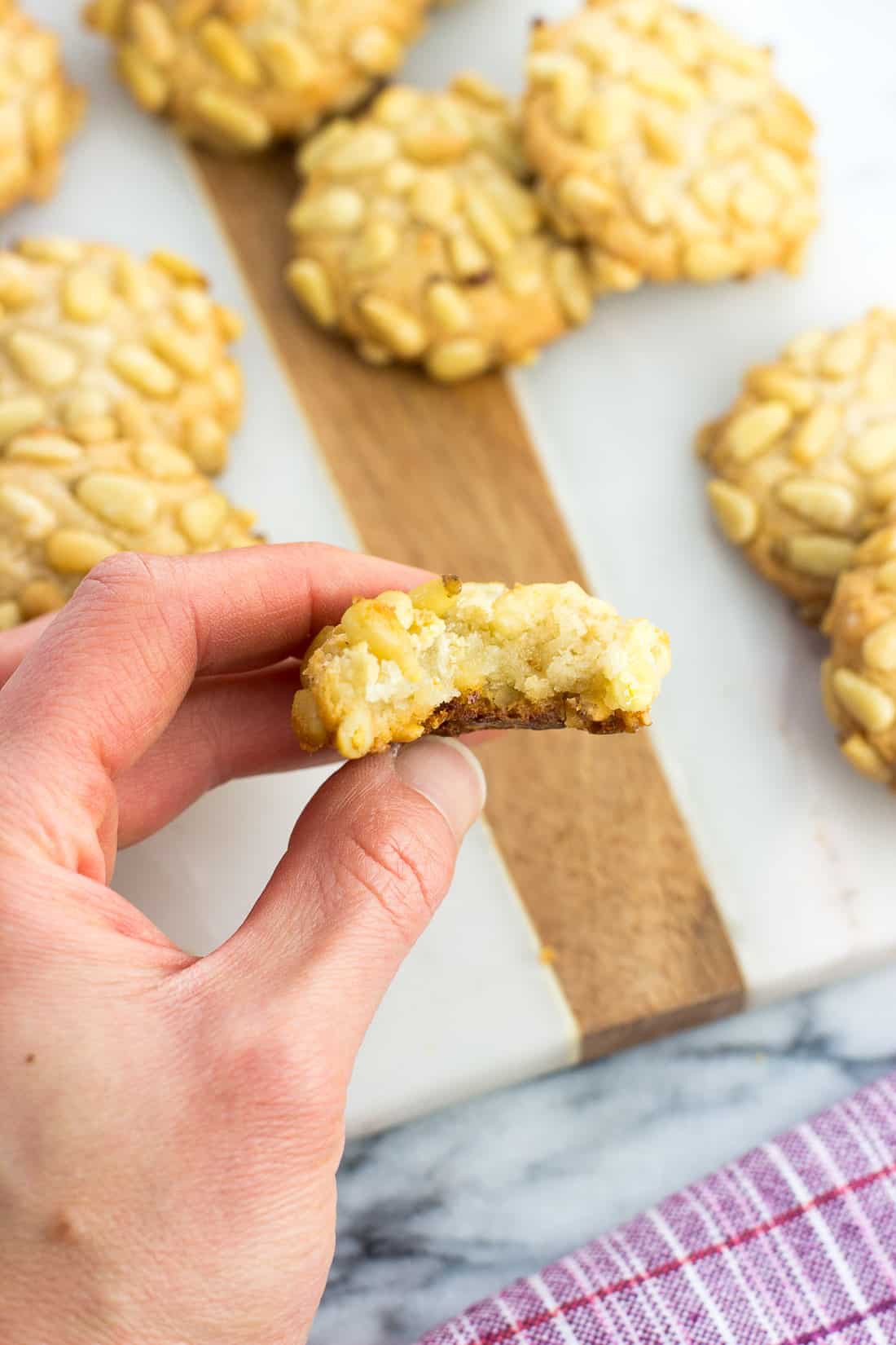 A hand holding a pignoli cookie with a bite taken out of it.