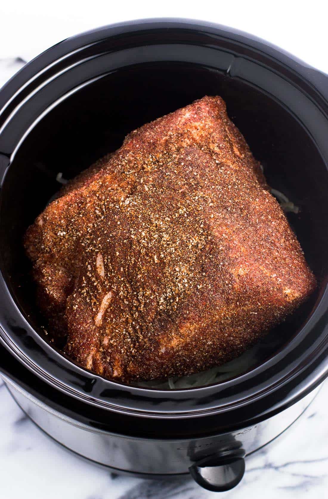 A seasoned Boston butt on a bed of sliced onion in the crock pot before being cooked