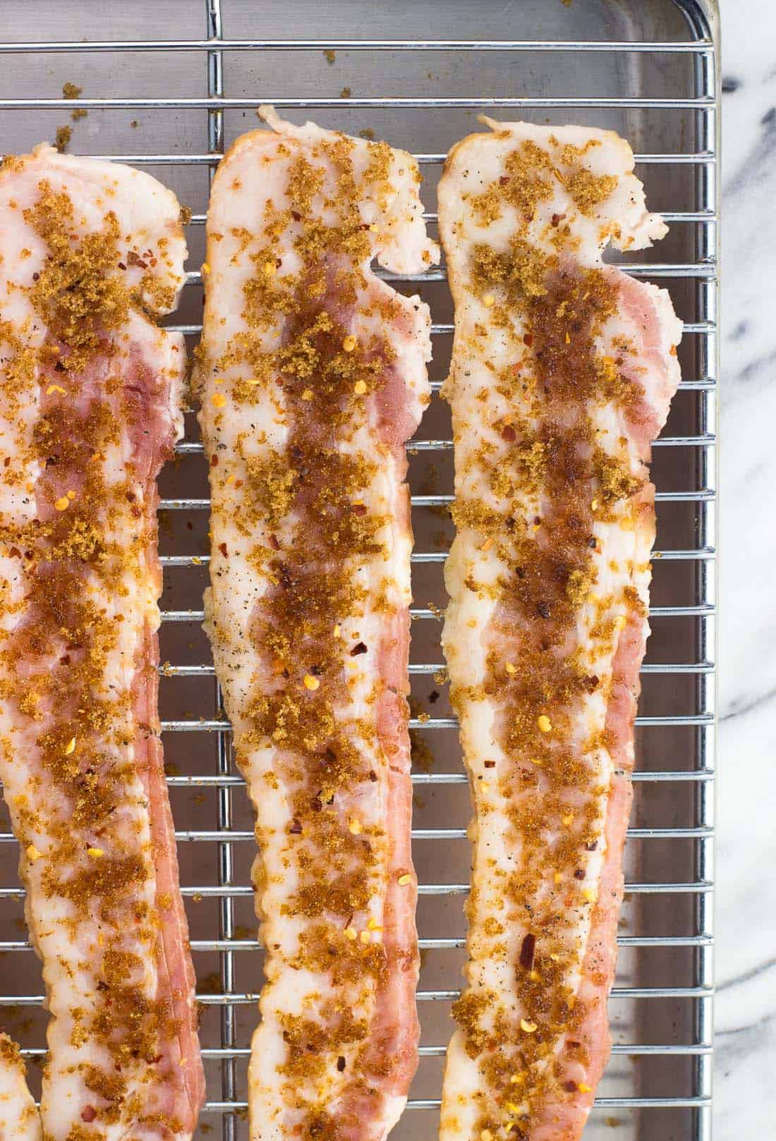 Uncooked bacon sprinkled with pepper and brown sugar on a wire rack.