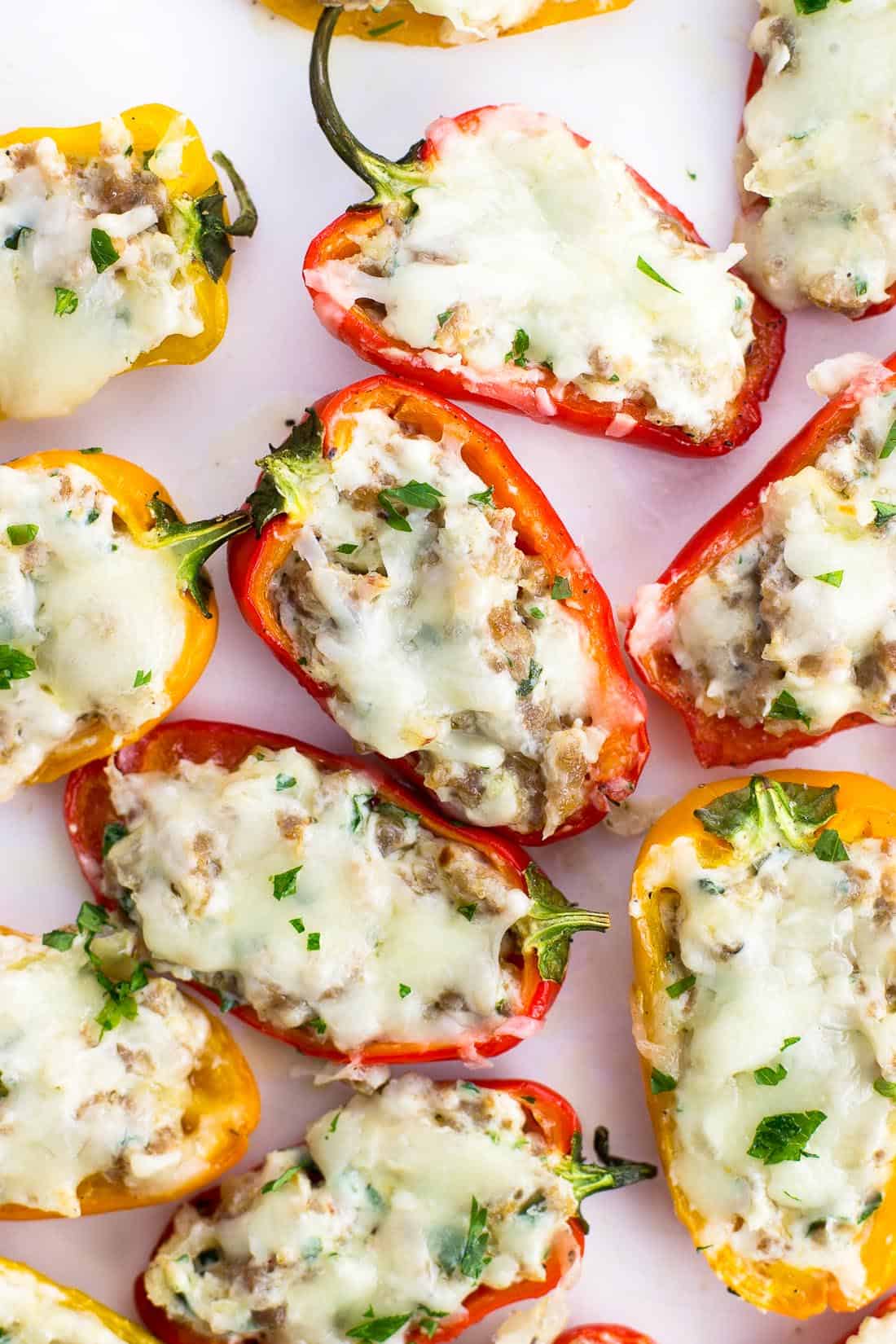 Sausage stuffed mini peppers on a serving plate sprinkled with fresh herbs.