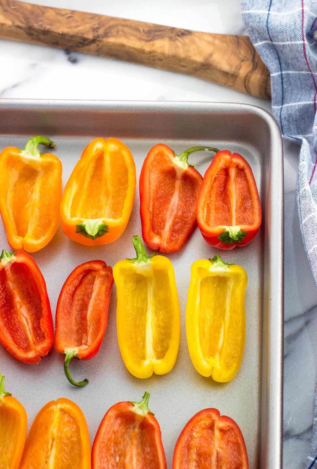 Mini sweet peppers cut into halves with the seeds removed, cut-side up on a baking sheet.